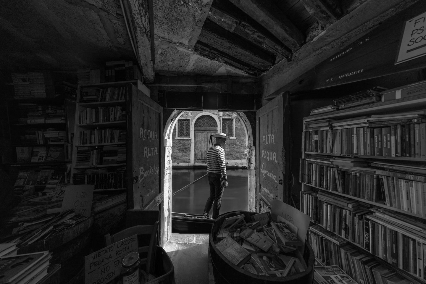 Venice gondolier passing behind Libreria Acqua Alta, black and white long exposure photograph, Venice, Italy.
