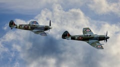 Two WWII Supermarine Spitfires, EP120 and RM927, flying in formation through billowing clouds, the pilot of RM927 flashing a V for Victory salute. (thumbnail 3)