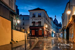 Le Consulat on rue Norvins in Montmartre, Paris, at blue hour, with glowing street lamps, rain-wet cobblestones, shuttered shopfronts, and the dome of Sacré-Cœur beneath a starry sky; limited edition fine art photograph by Sherry Keene. (thumbnail 3)